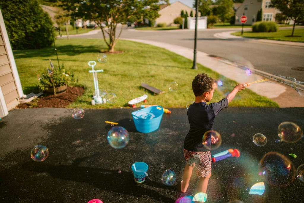 photo of kid playing with bubbles during the summer in front yard