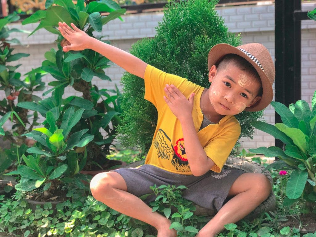 a photo of a child posing in a quirky way with leaves behind him
