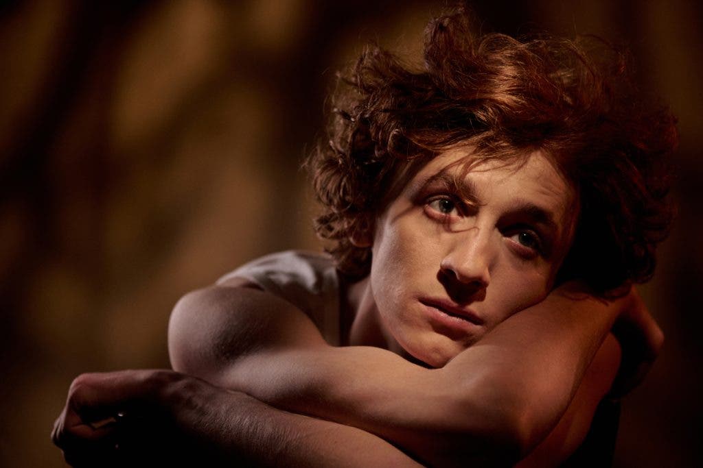 Medium close up of red haired man dressed in white t-shirt lying on own hands and immersed into thoughts