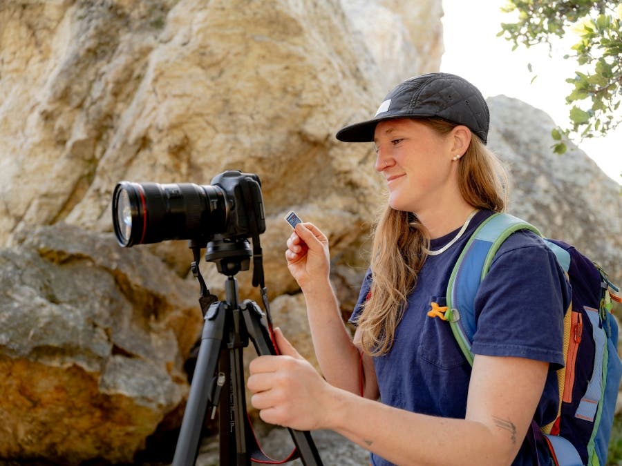 female adventure photographer smiles as she holds SD card and camera tripod