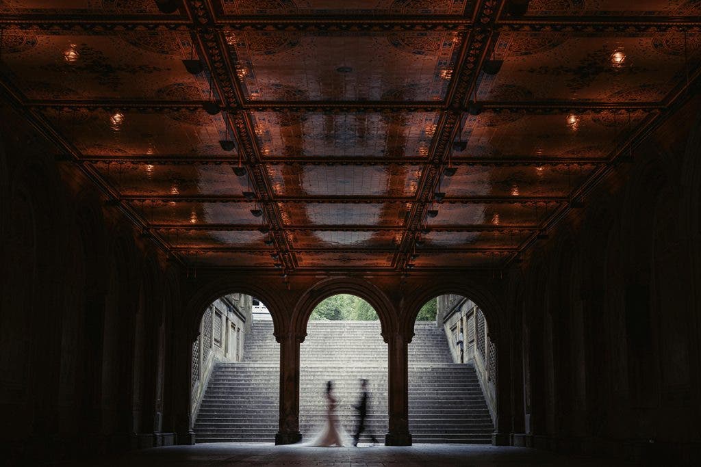A wedding couple captured in motion while walking through an ornate, vaulted stone tunnel with dramatic ceiling tiles, shot by Susan Stripling.
